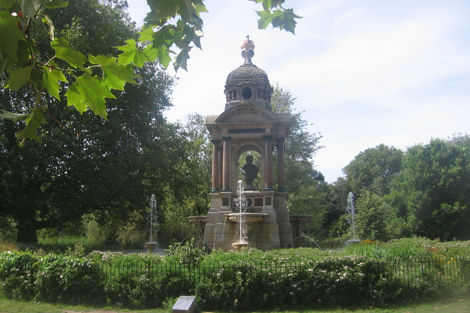 Green Sarphatipark with a pond and trees against a backdrop of residential buildings.