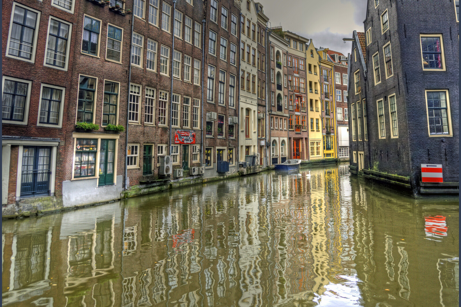 A narrow canal in Amsterdam, surrounded by old brick houses reflected in the water.