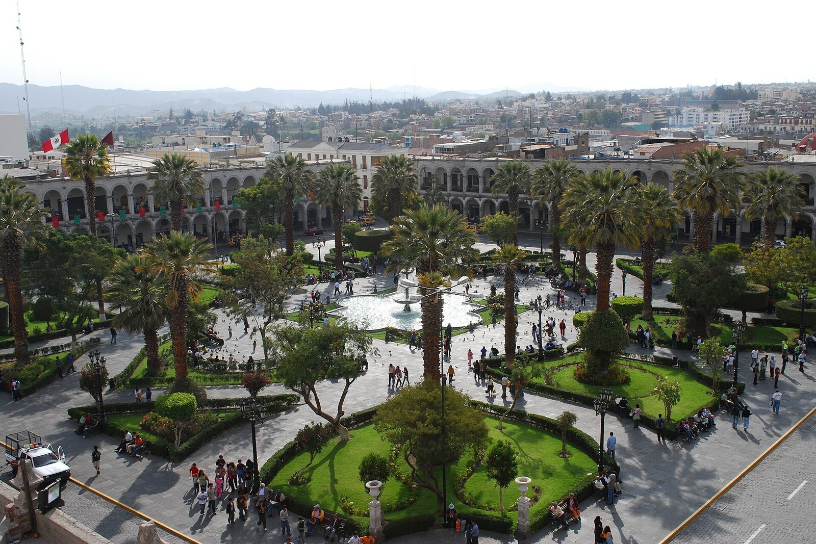 General view of Plaza de Armas in Arequipa: fountain, palm trees, and white arcades.