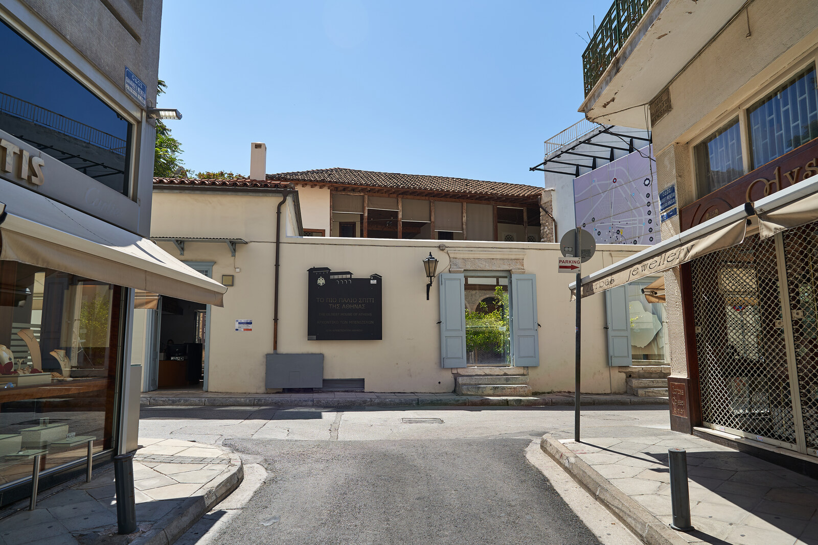 An old two-story mansion with a wooden canopy and stone arches on a street in Plaka