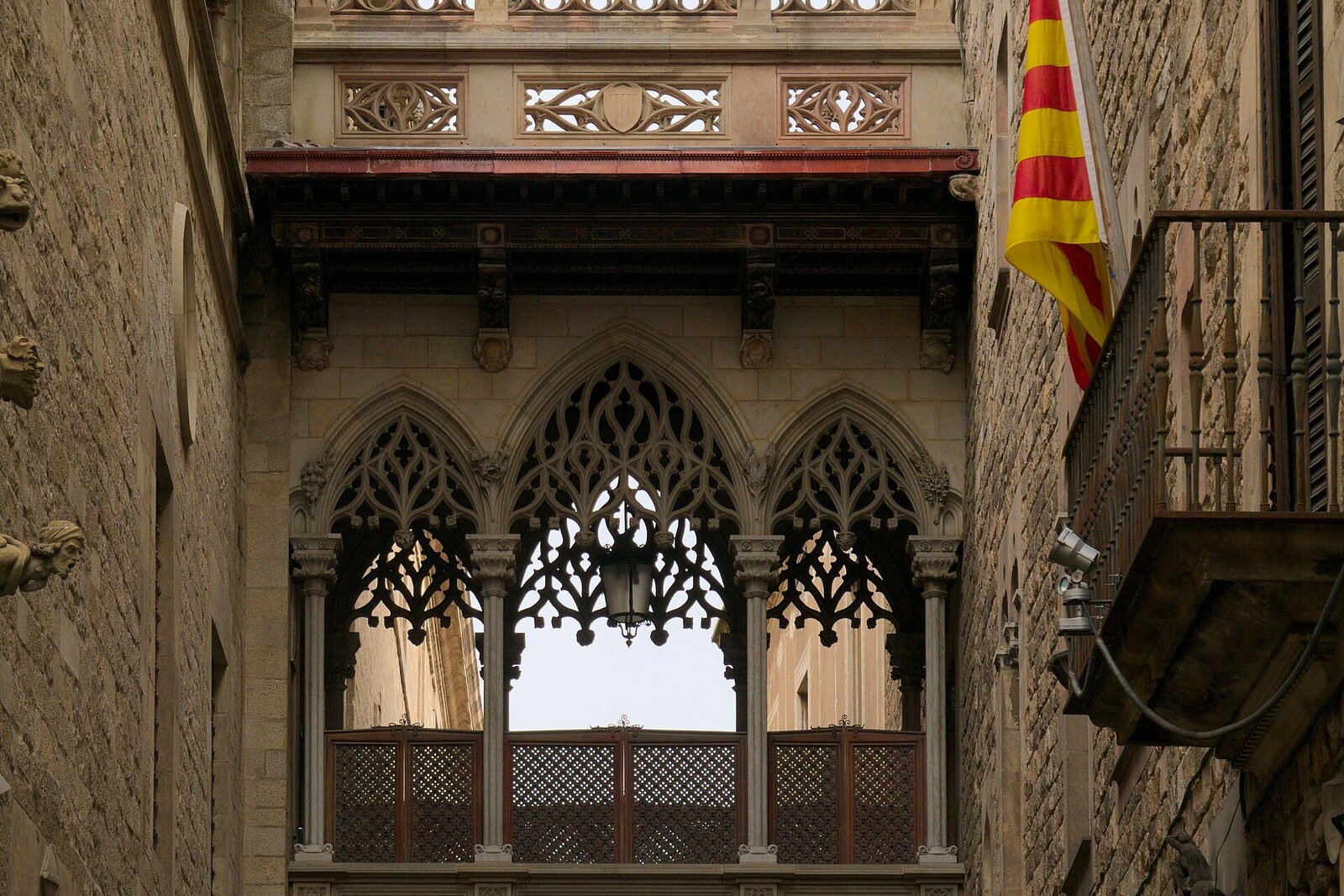 A Neo-Gothic stone bridge connects buildings above a narrow street in Barcelona