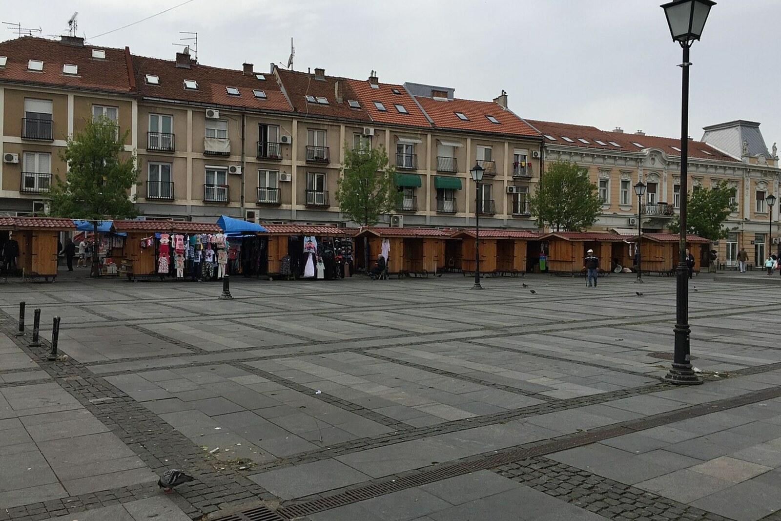 People buy vegetables and fruit at a market on a square with Baroque houses.