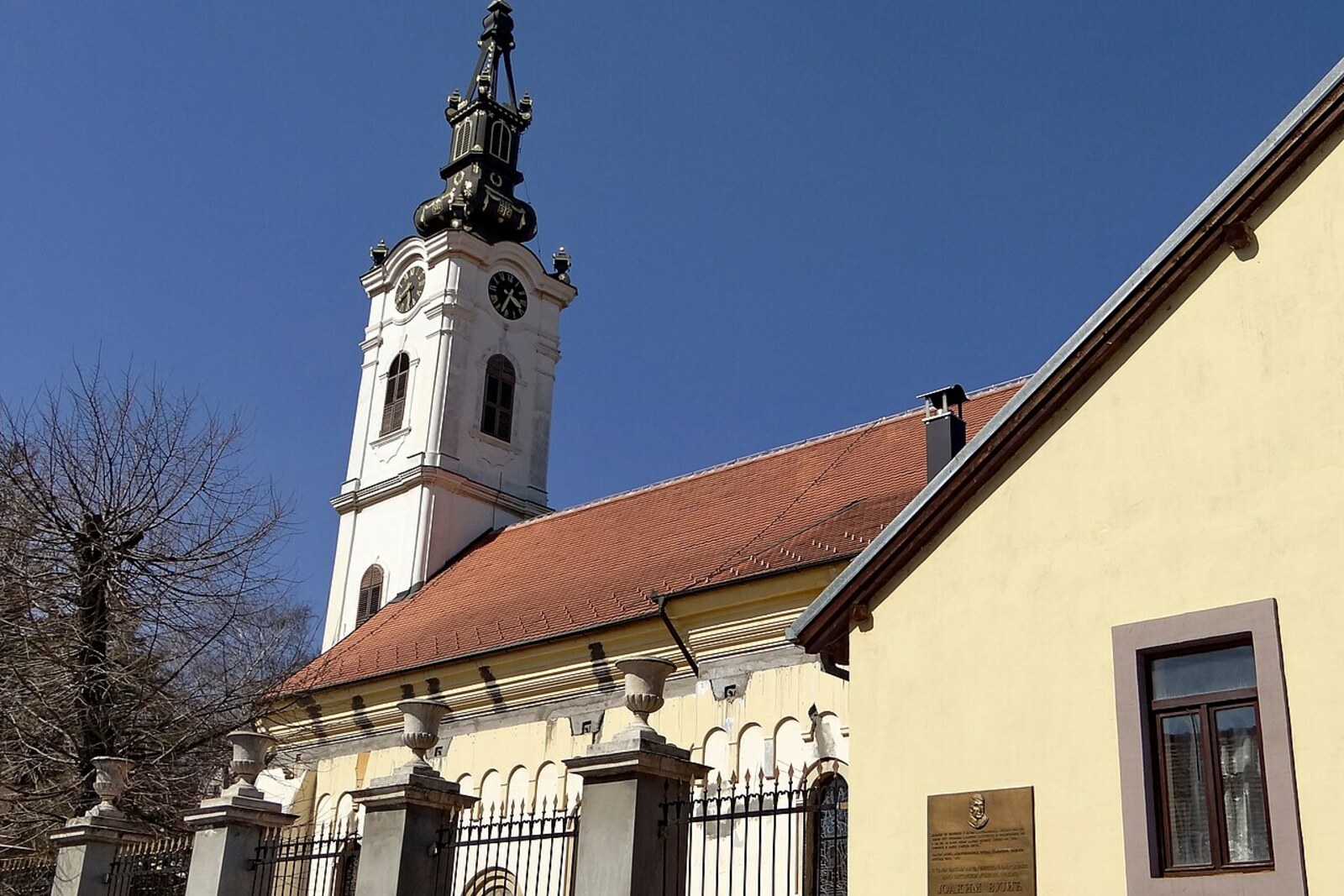 A church with a tall bell tower, surrounded by trees and old houses.