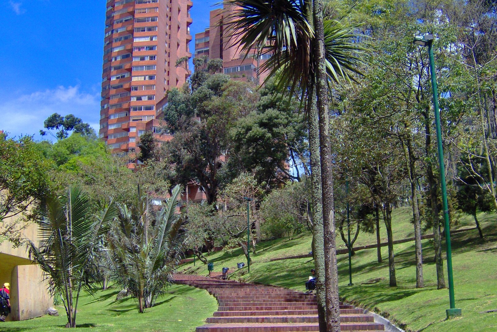 A green park with paths and trees, with brick towers rising behind them