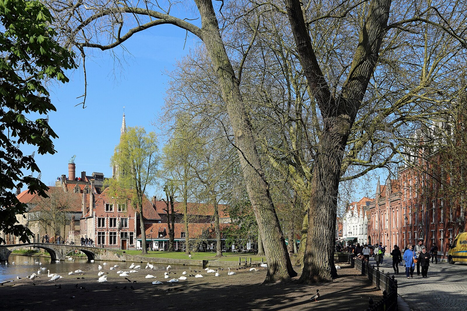 Wijngaardplein square with a carriage, the beguinage's white gate arch, and a lock house in Bruges