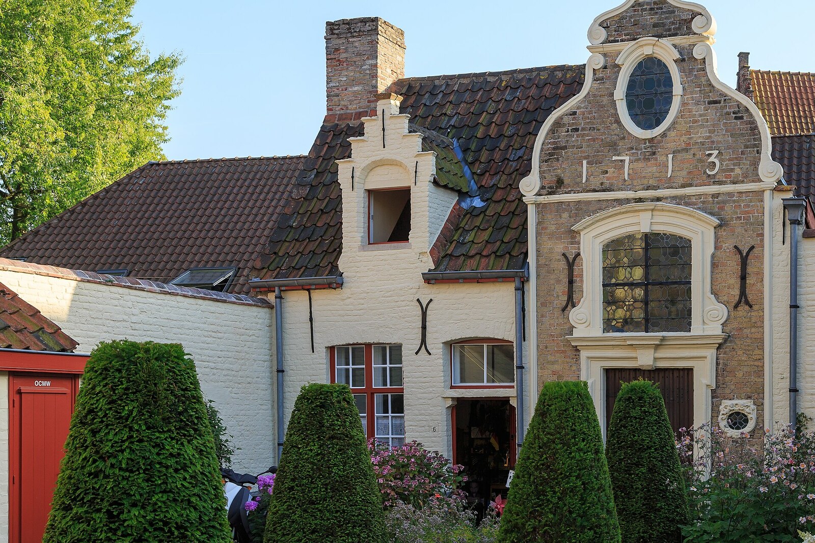 The white De Vos Almshouse in Bruges, with a Baroque gable and the date 1713 on the façade