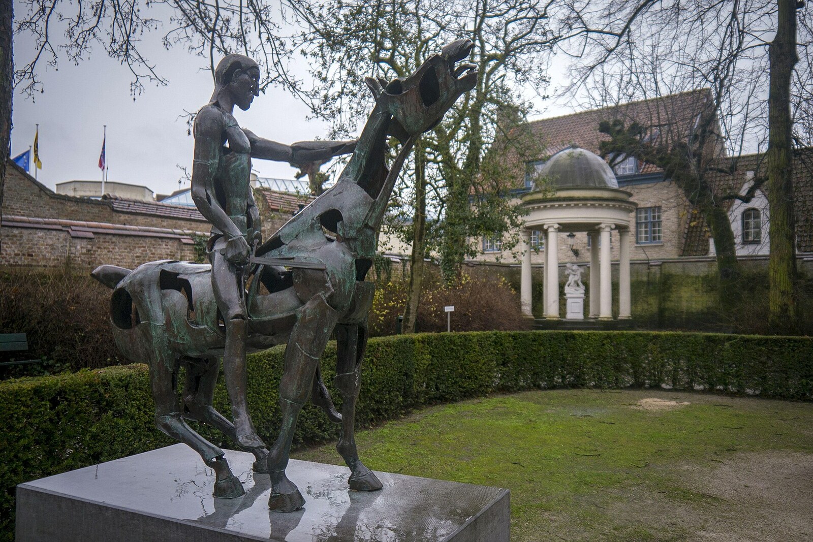 A bronze rider with a raised hand among trees.