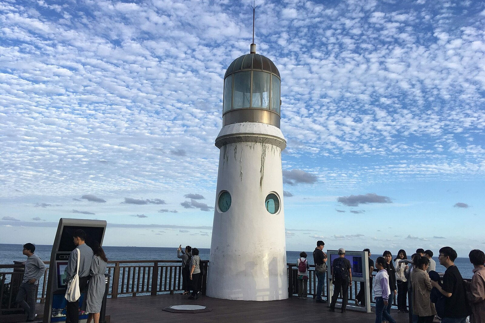 White Dongbaekseom Lighthouse on a rock above the sea, with a panorama of the Busan coast.