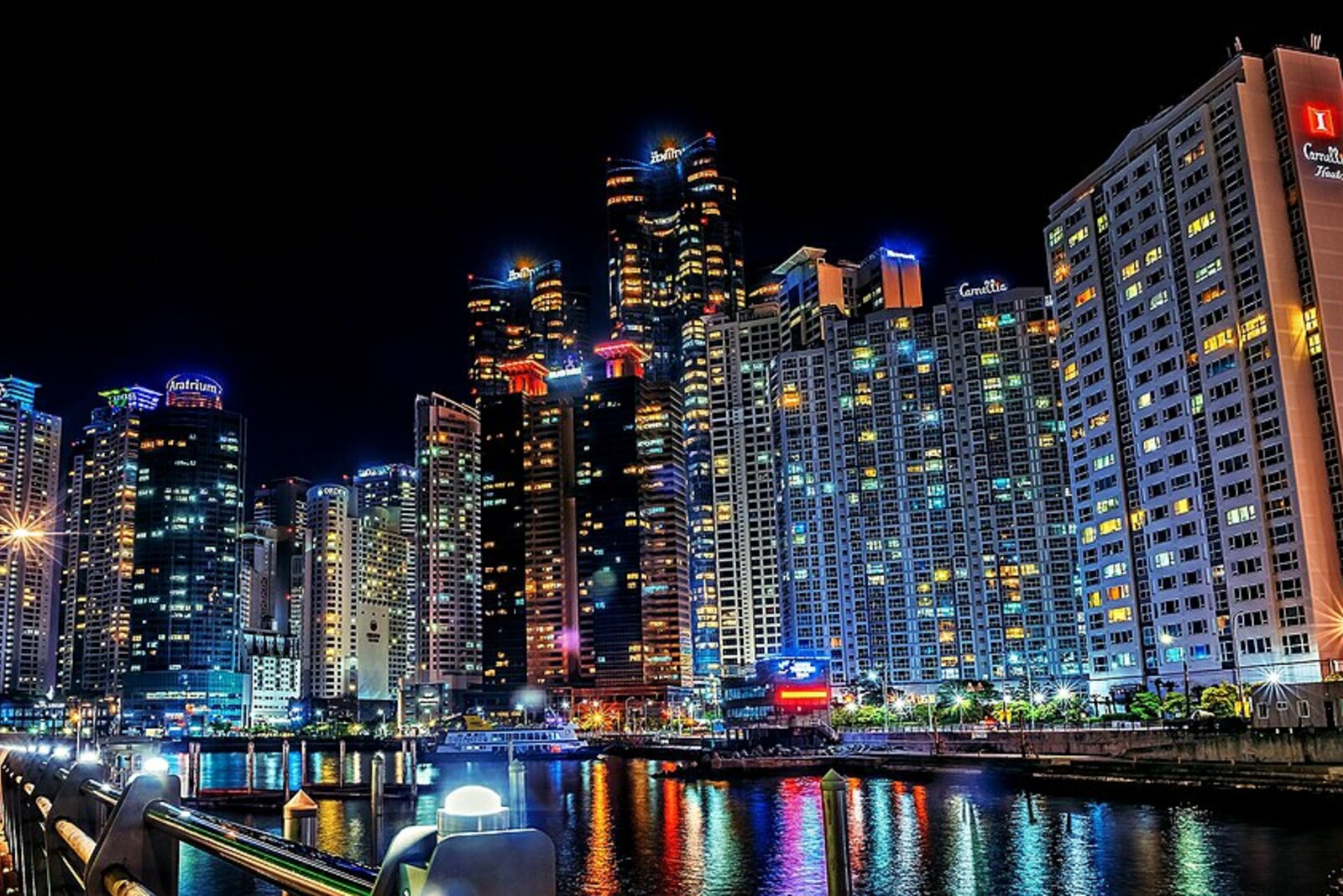 Nighttime waterfront at The Bay 101: reflections of Marine City's lights in the water and the pedestrian edge of Haeundae Harbor.