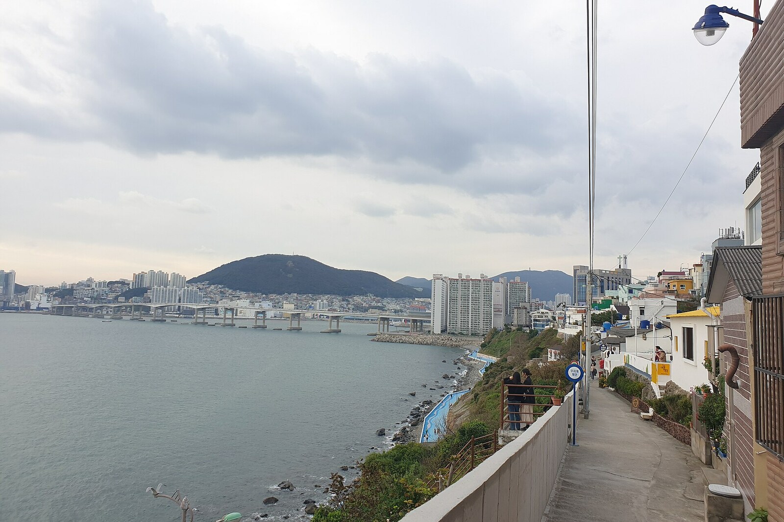 A road along white houses on a cliff, overlooking the bay.