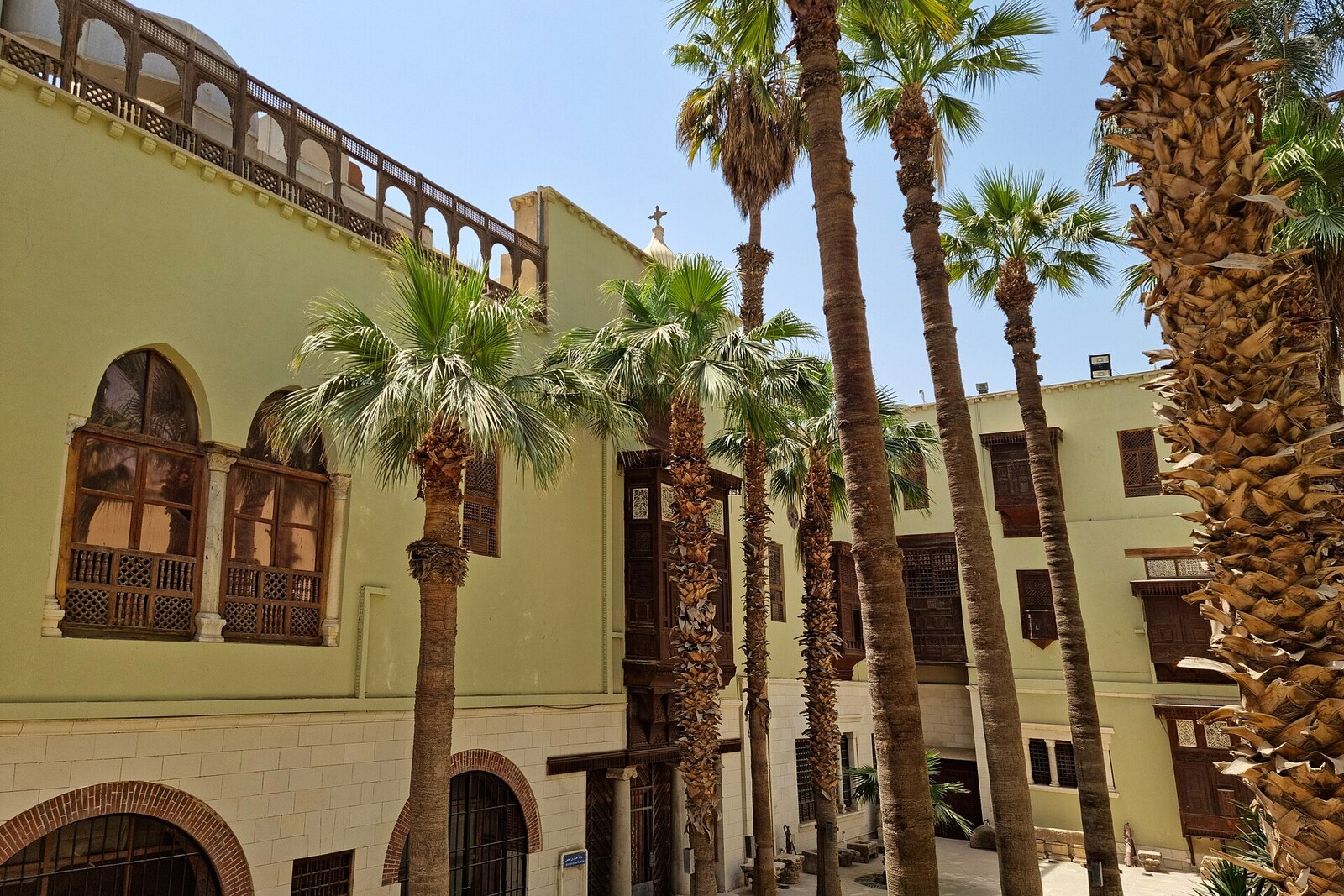 A courtyard with palm trees and the facade of the Coptic Museum in Old Cairo