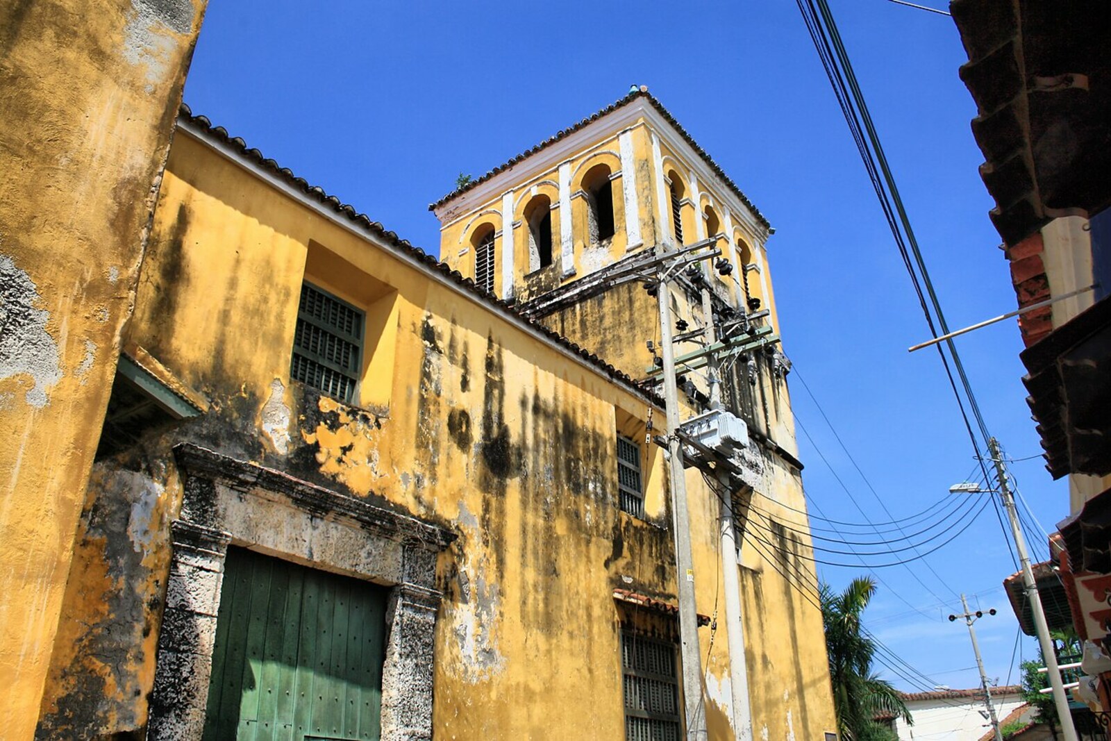 Yellow façade of Iglesia de la Santísima Trinidad with white columns and a bell tower