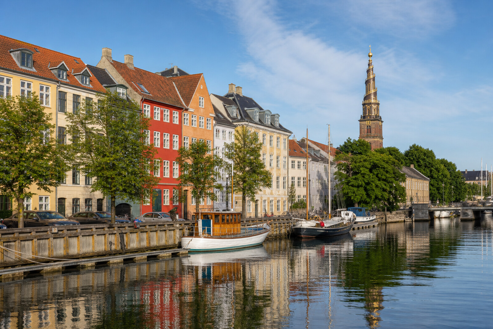 Colorful houses along the canal and a golden church spire in Christianshavn on a sunny day.