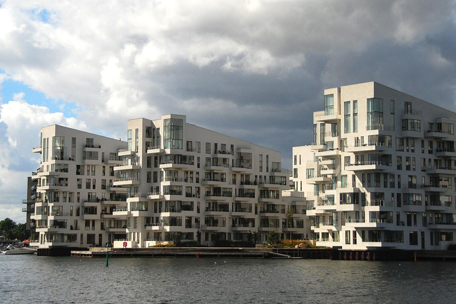 White U-shaped Havneholmen buildings on the water, with wooden footbridges and boats in the canals