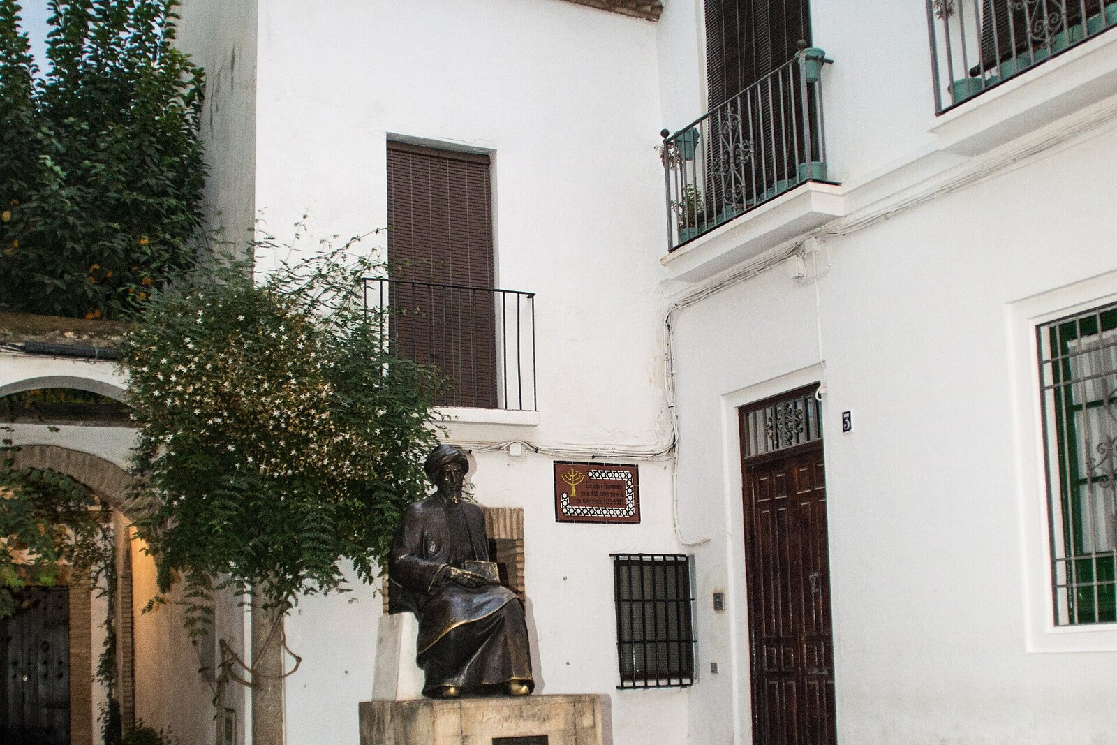 A seated bronze Maimonides on a plinth in the white Plaza de Tiberíades.
