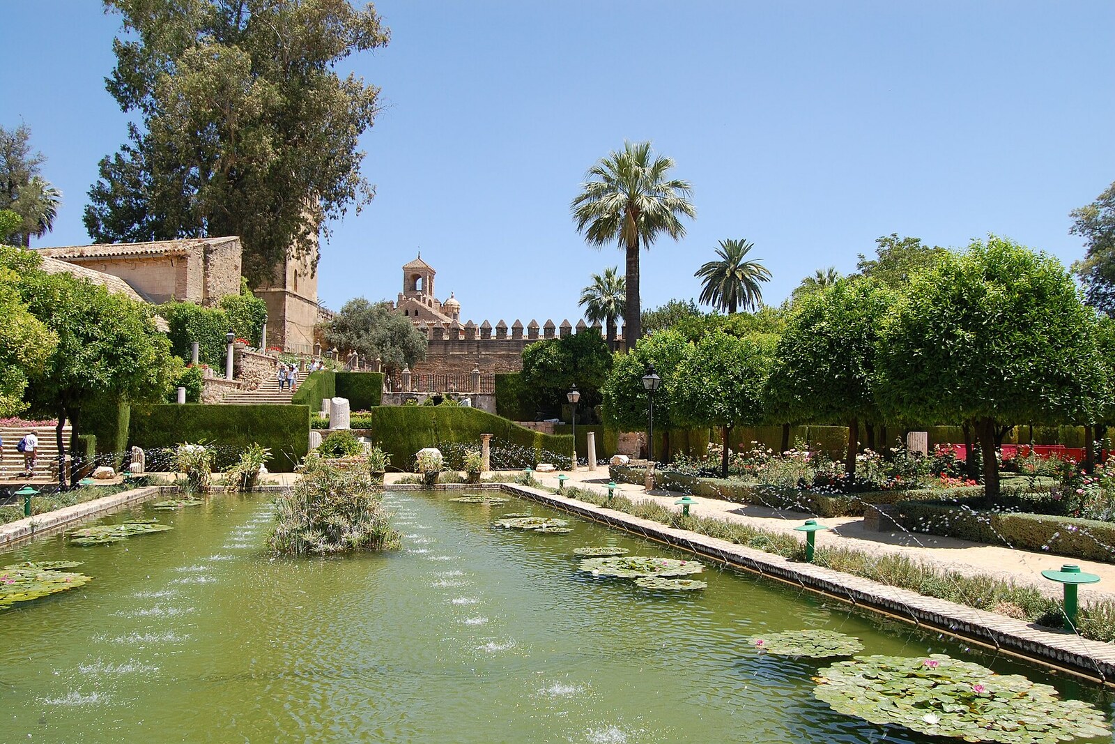 A rectangular pond, trimmed greenery, and a crenellated wall in the gardens of the Alcázar.