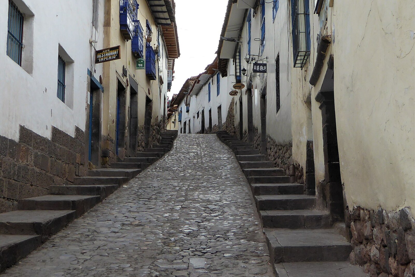 Steep Cuesta de San Blas street with stone walls and workshop doors
