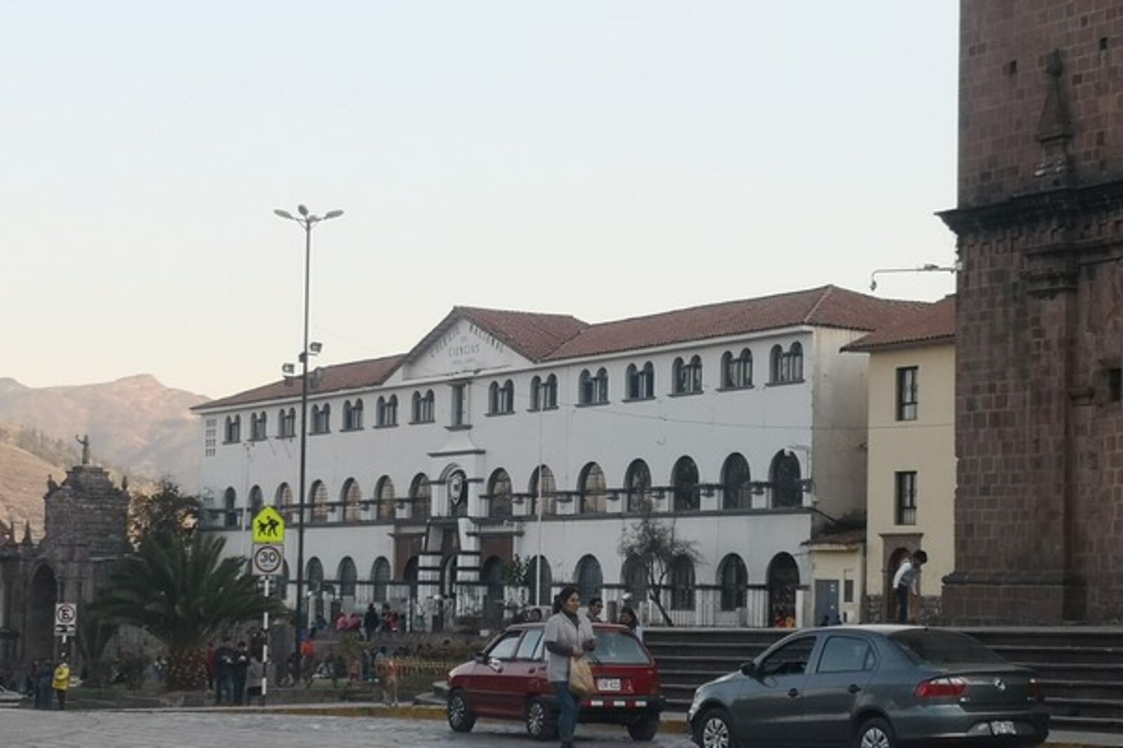 Façade of the Ciencias school in Cusco, with columns and the Santa Clara Arch in the distance.