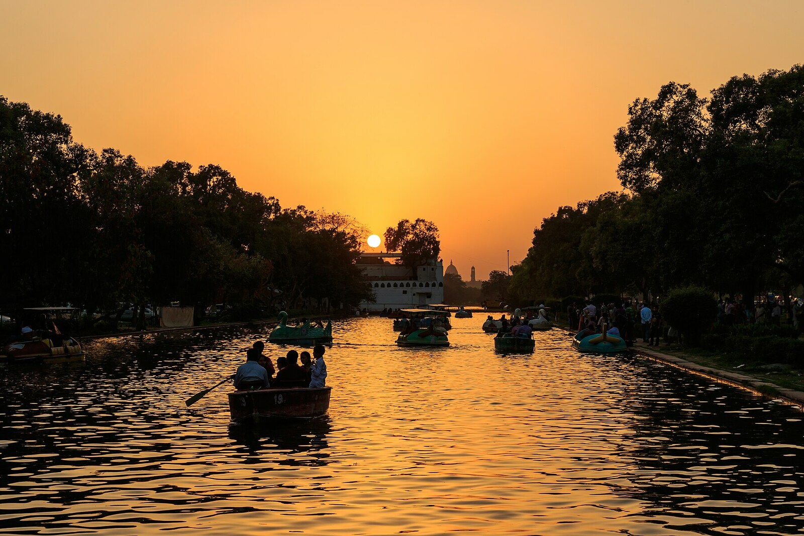 Sonnenuntergang über einem Kanal des Kartavya Path mit der Spiegelung von Lampen und einer Allee.