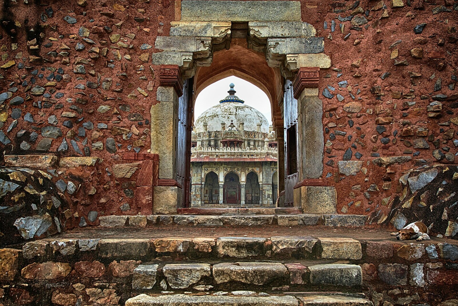 Isa Khan's octagonal tomb, seen through an arched passage against a blue sky.