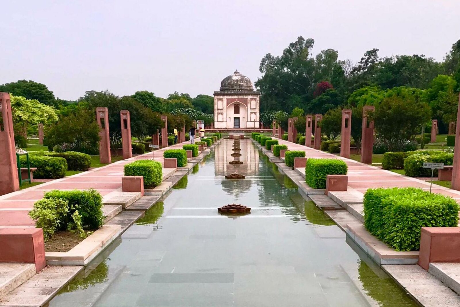 A long water channel with green plantings in Sunder Nursery Park, with a domed tomb on the horizon.