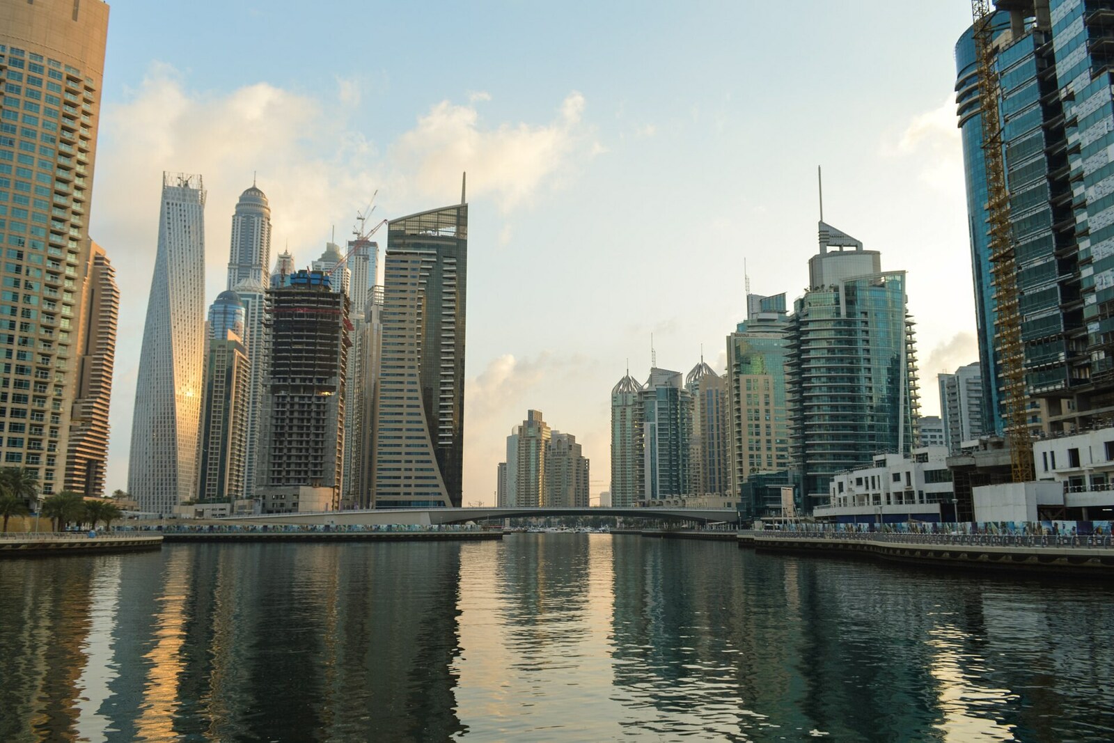 Abendlicher Blick auf die Dubai Marina Walk mit Palmen, Booten und Spiegelungen der Gebäude.