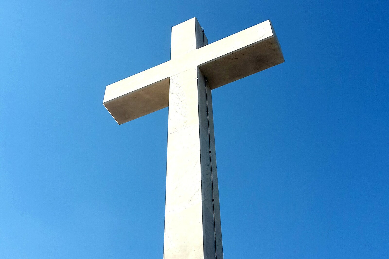A tall white stone cross on Mount Srđ, standing on a platform overlooking the sea