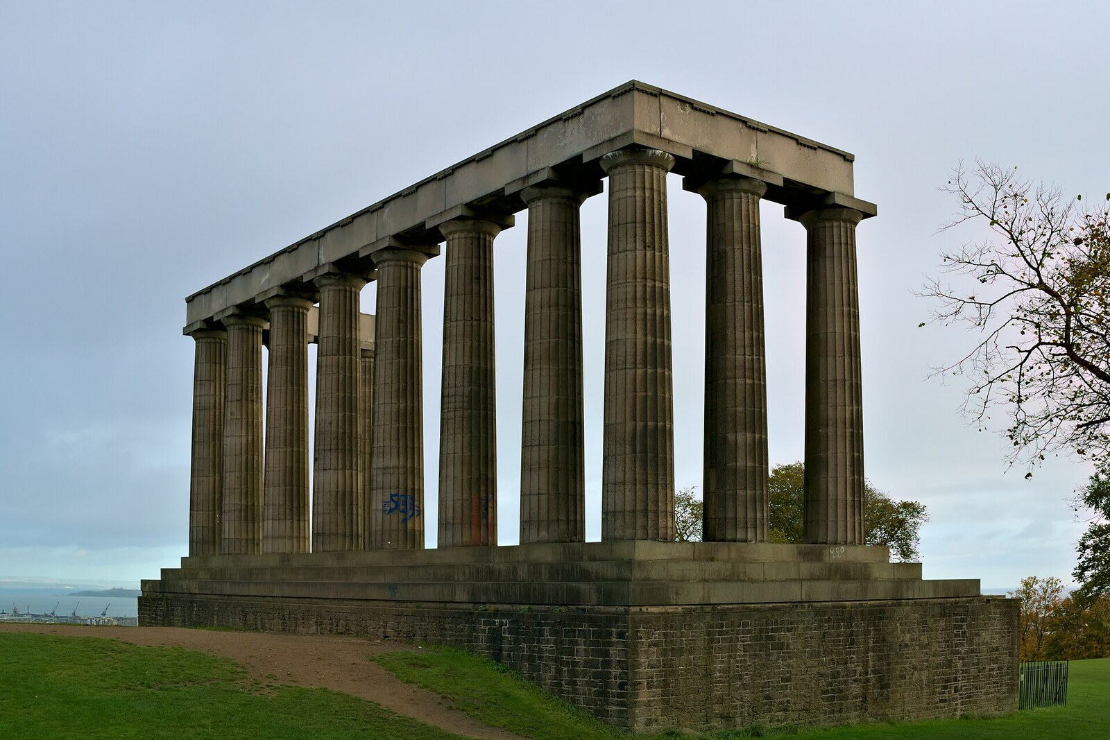 A row of massive stone columns on a hill overlooking the city; green grass and sky surround them.