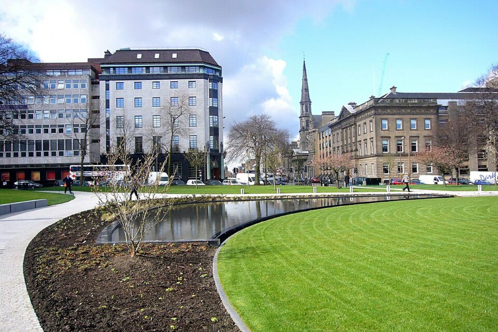 View of St Andrew Square: a green lawn and a pond in the foreground, with neoclassical buildings behind them.