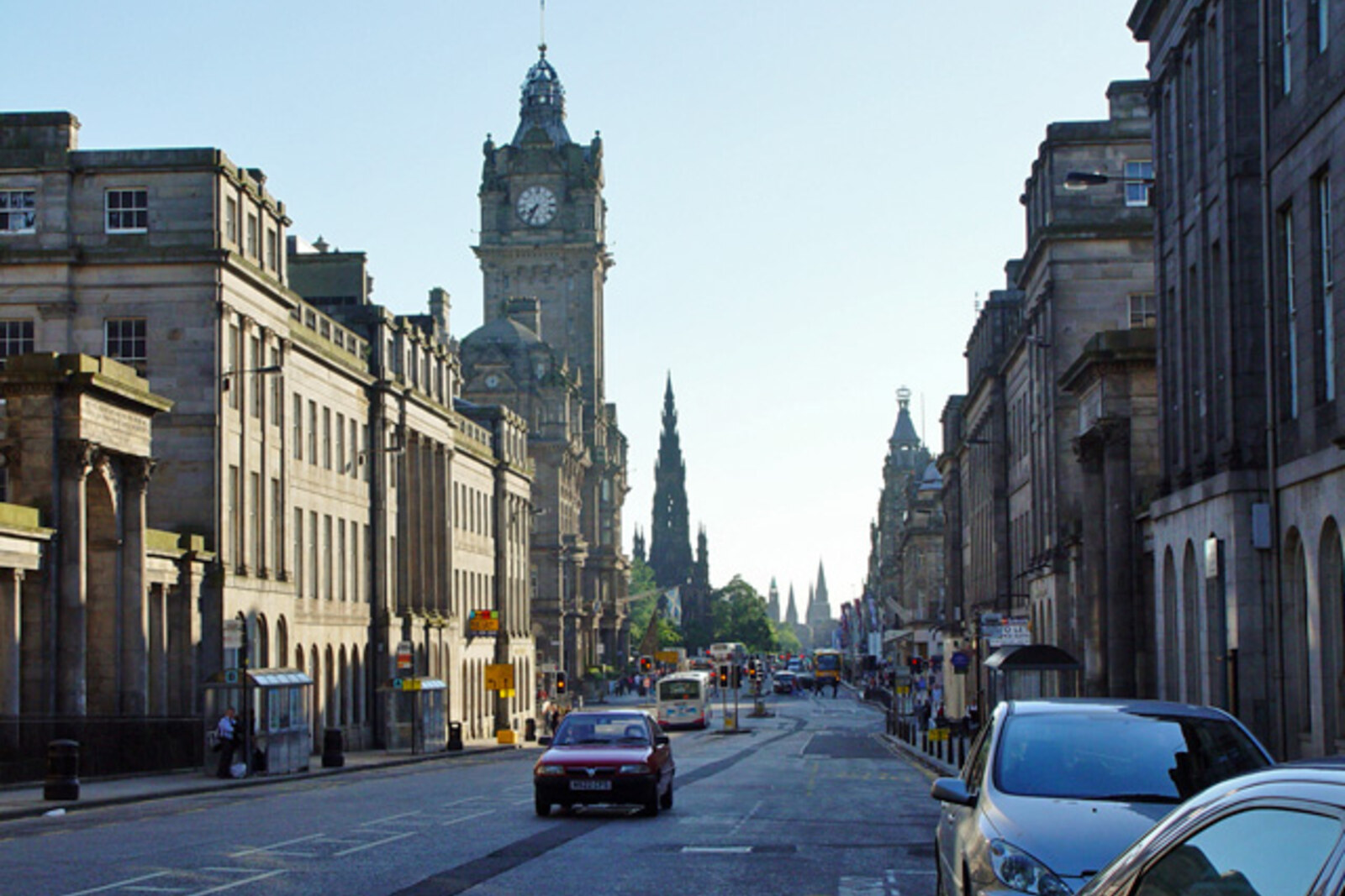 Princes Street with tall stone buildings, a hotel tower, and the spire of a monument on the horizon.