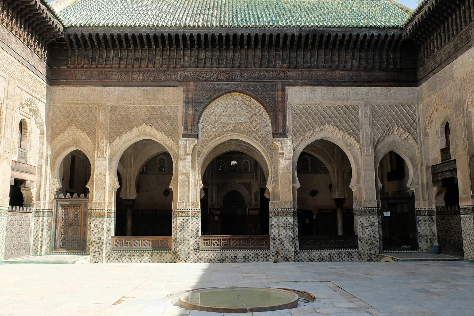 The courtyard of Bou Inania Madrasa with a round fountain and a carved prayer façade.
