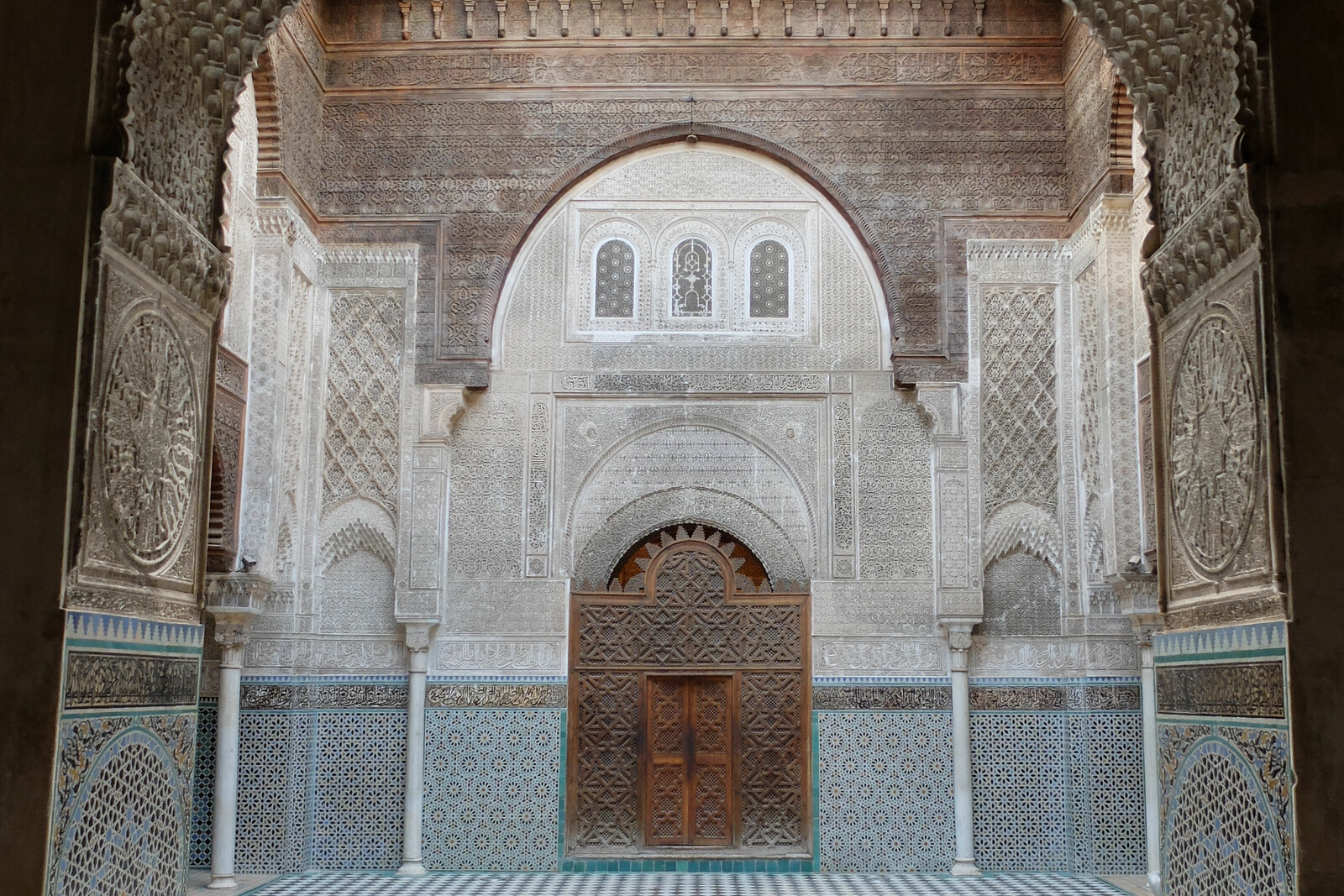 The courtyard of Al-Attarine Madrasa, with a carved arch, a fountain, and a black-and-white tiled floor.