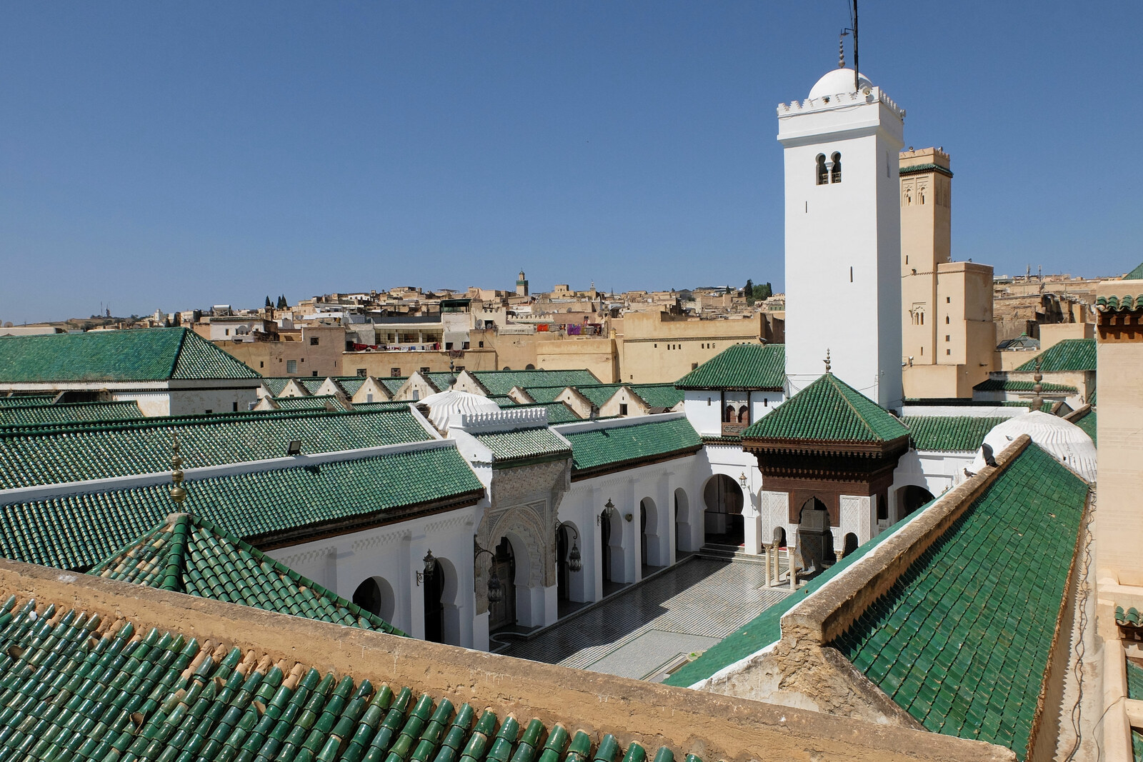 The green roofs and white minaret of al-Qarawiyyin, seen from above over the inner courtyard.
