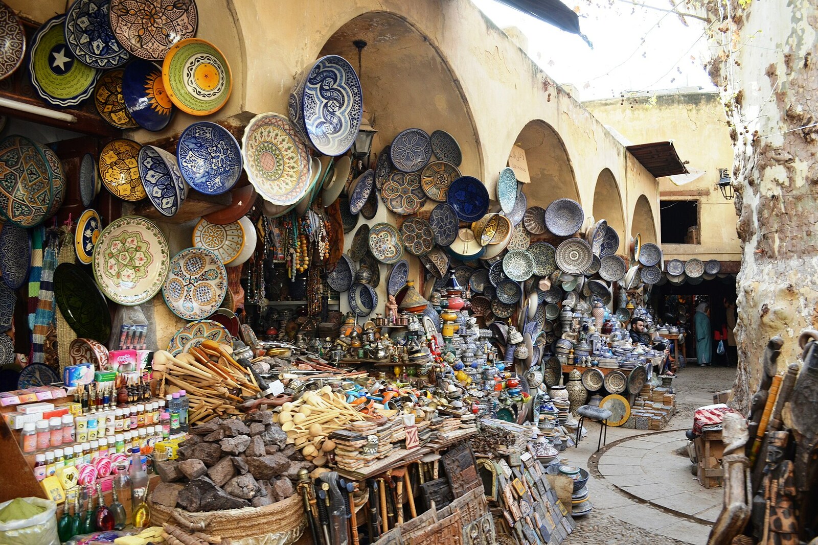 A square with plane trees and rows of shops selling ceramics and herbs at Henna Souk