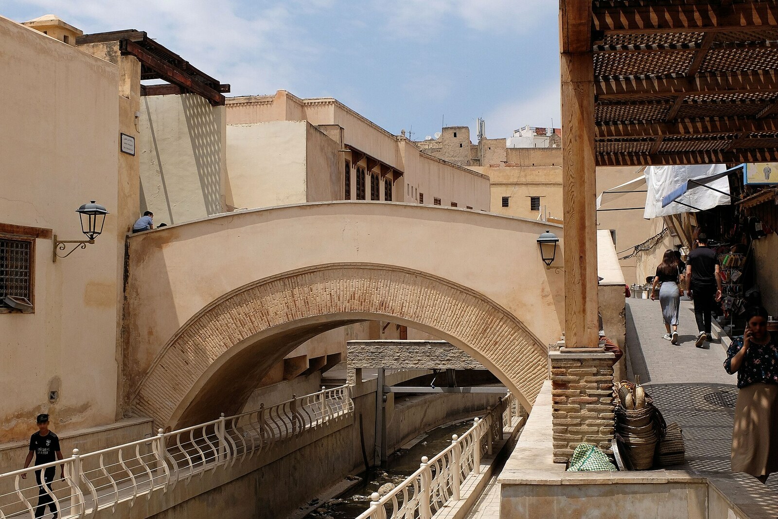 A stone bridge with arches over a green river in the Medina of Fez