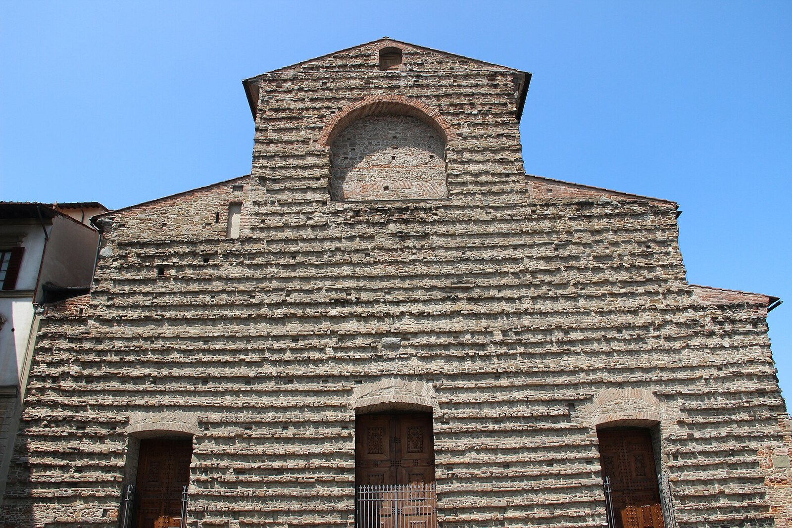 View of the unfinished stone facade of the Basilica of San Lorenzo, with the dome of the chapels at the side.