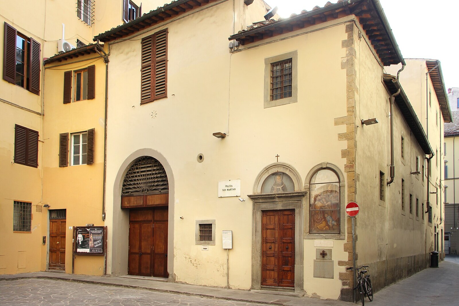 The stone façade of a small oratory, with a statue above its door, on Piazza San Martino.