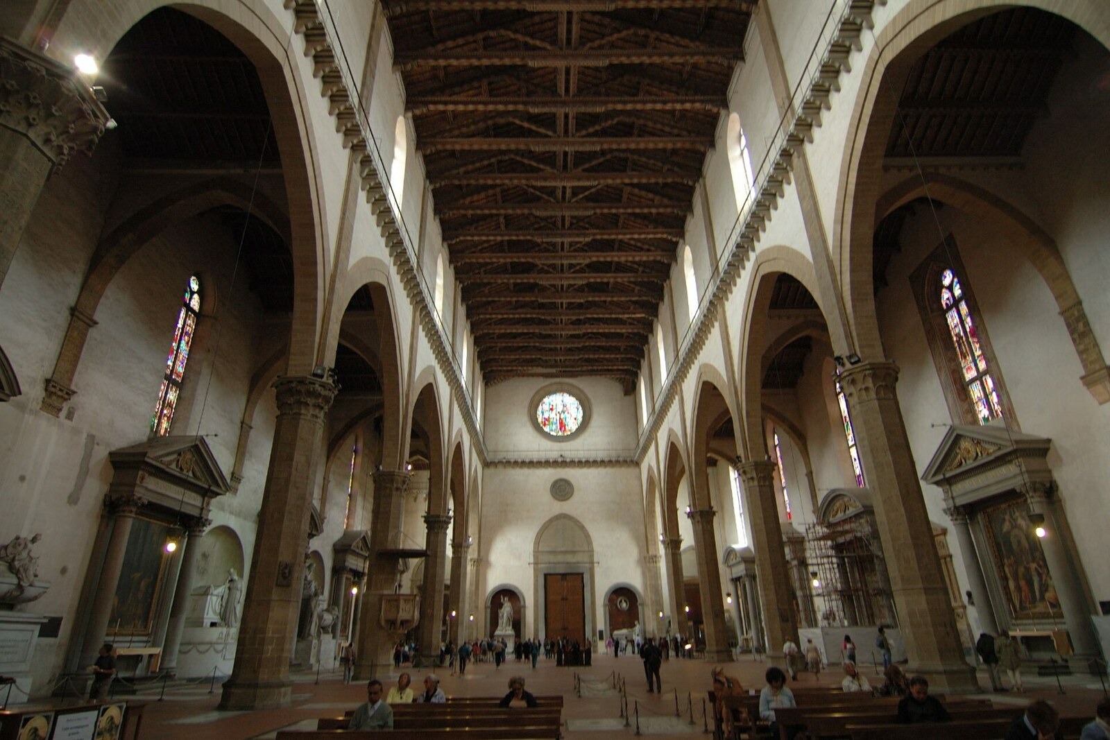 The bright interior of the Basilica of Santa Croce, with a long nave and a wooden ceiling.