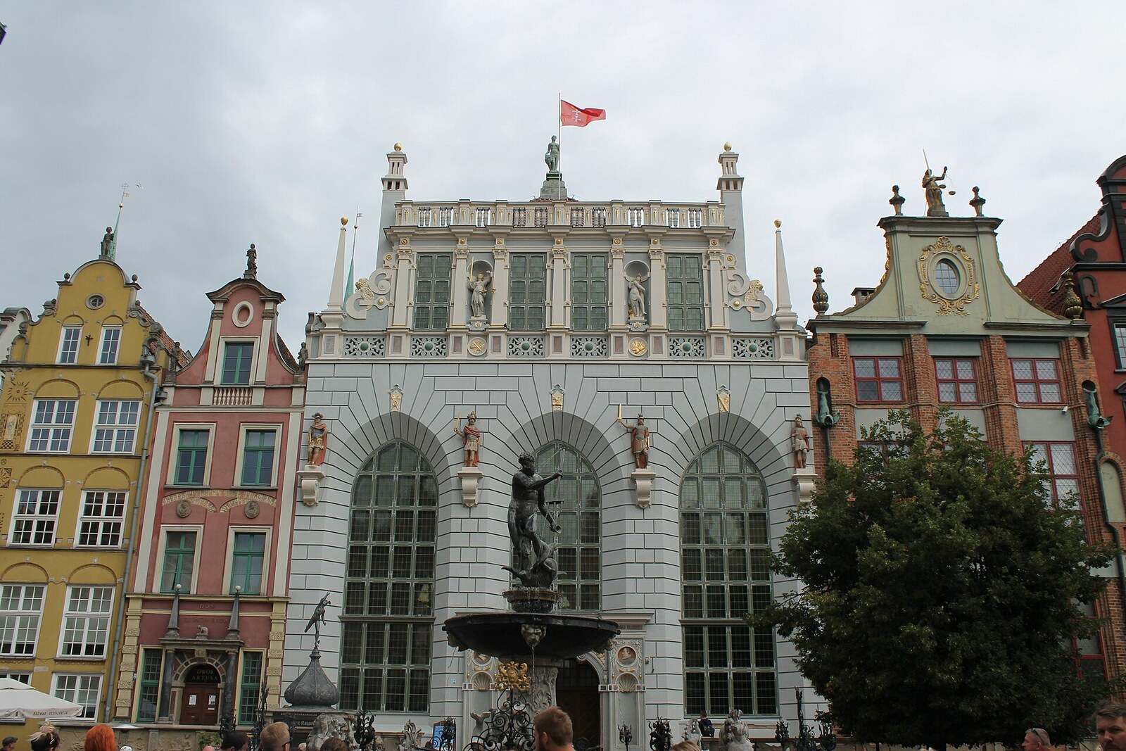 Bronze Neptune in front of the light-colored façade of Artus Court in Gdańsk.