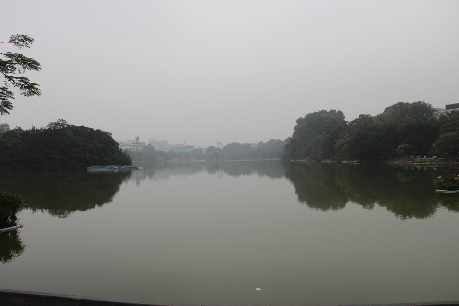 A wide daytime view of Hoan Kiem Lake from the shoreline.