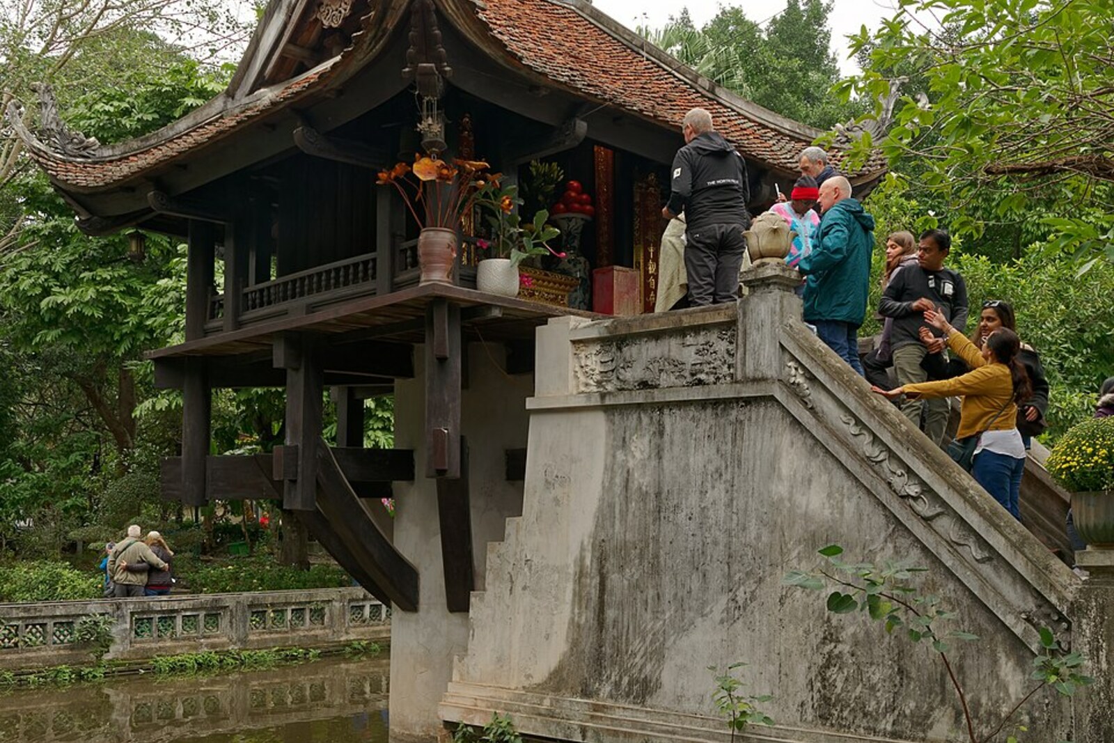 A small wooden pagoda raised on a single stone pillar above a pond.