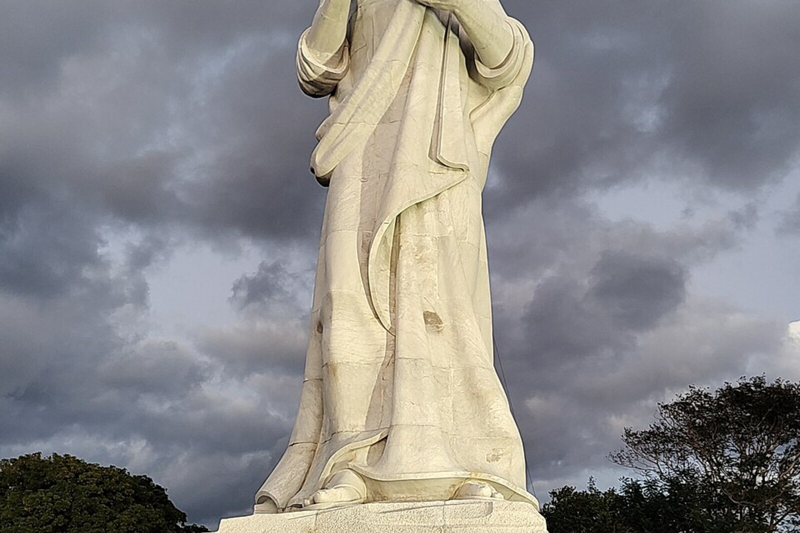 A tall white statue of Christ with outstretched arms on a hill