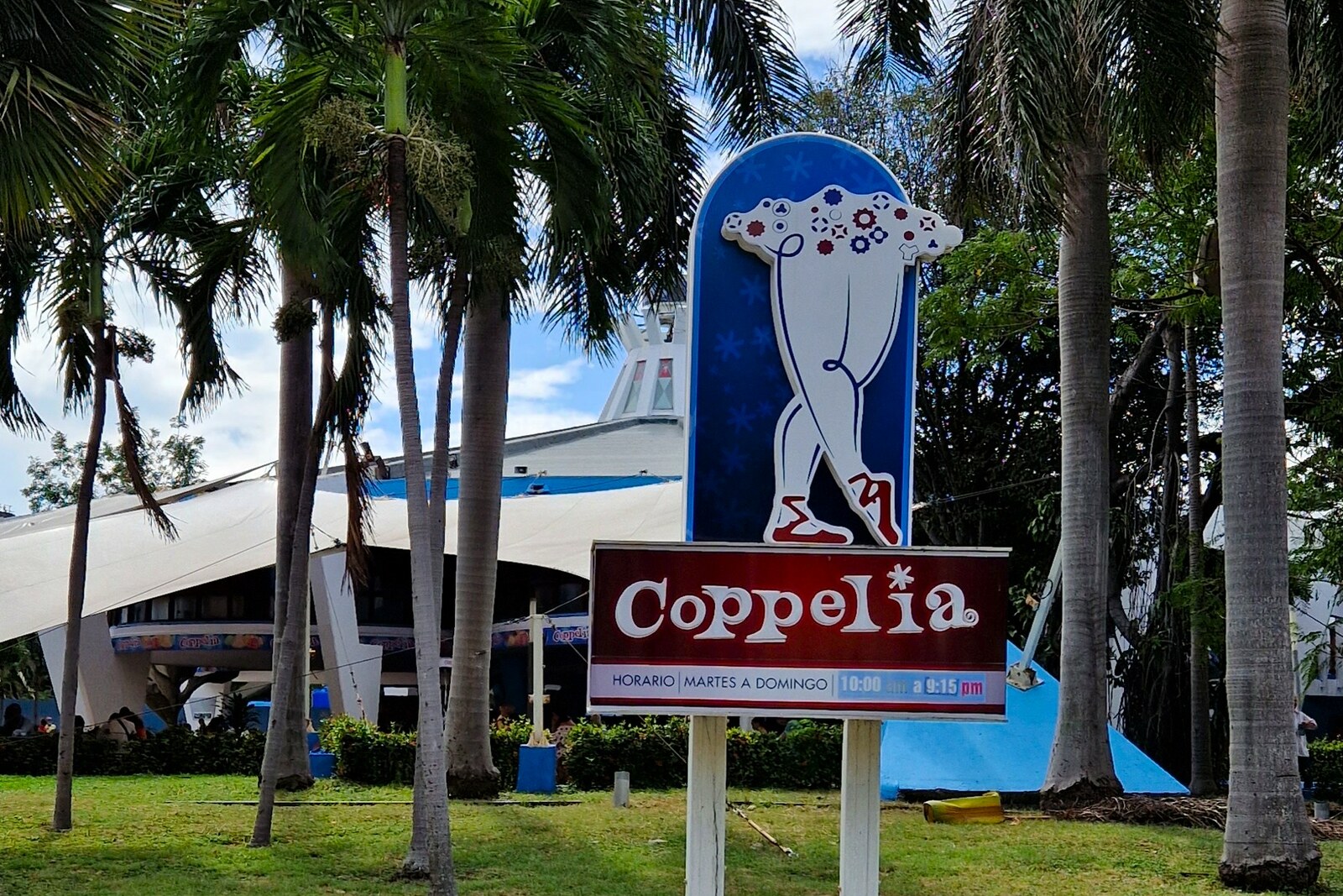 The round concrete pavilion of Coppelia Ice Cream Parlor is surrounded by trees; tables and visitors are visible through its glass walls.