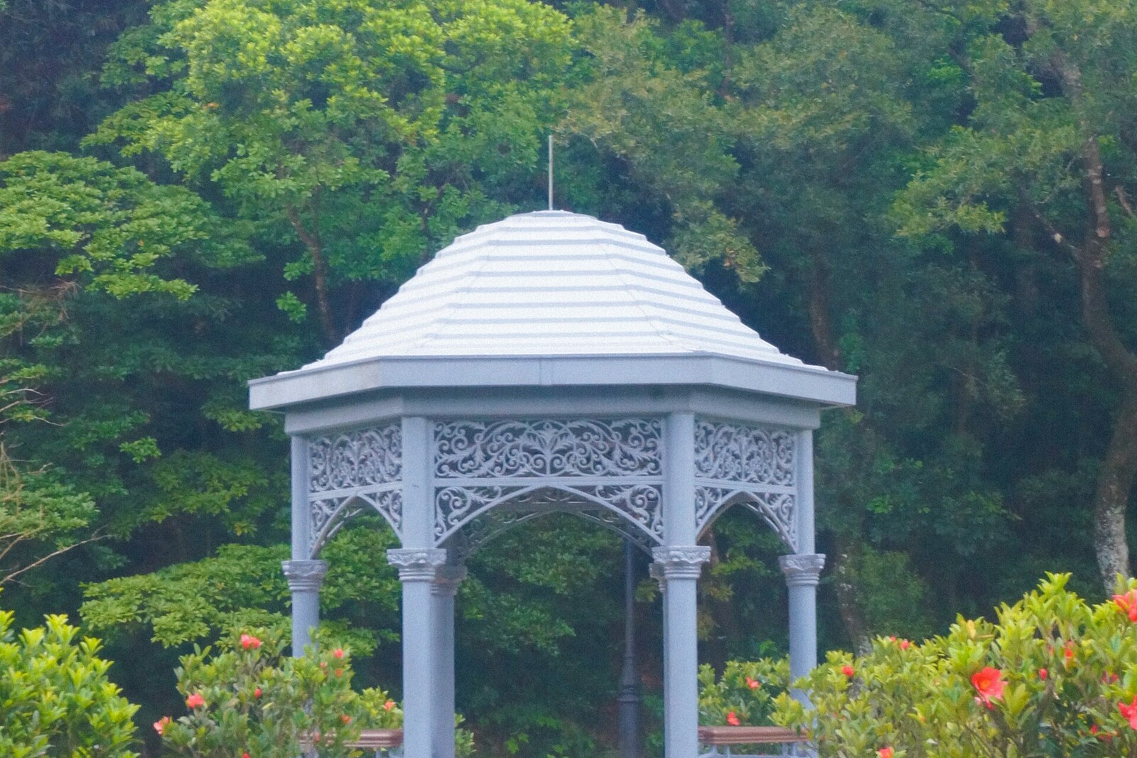 An elegant pavilion with a Chinese-style roof standing amid a green garden on a mountaintop.
