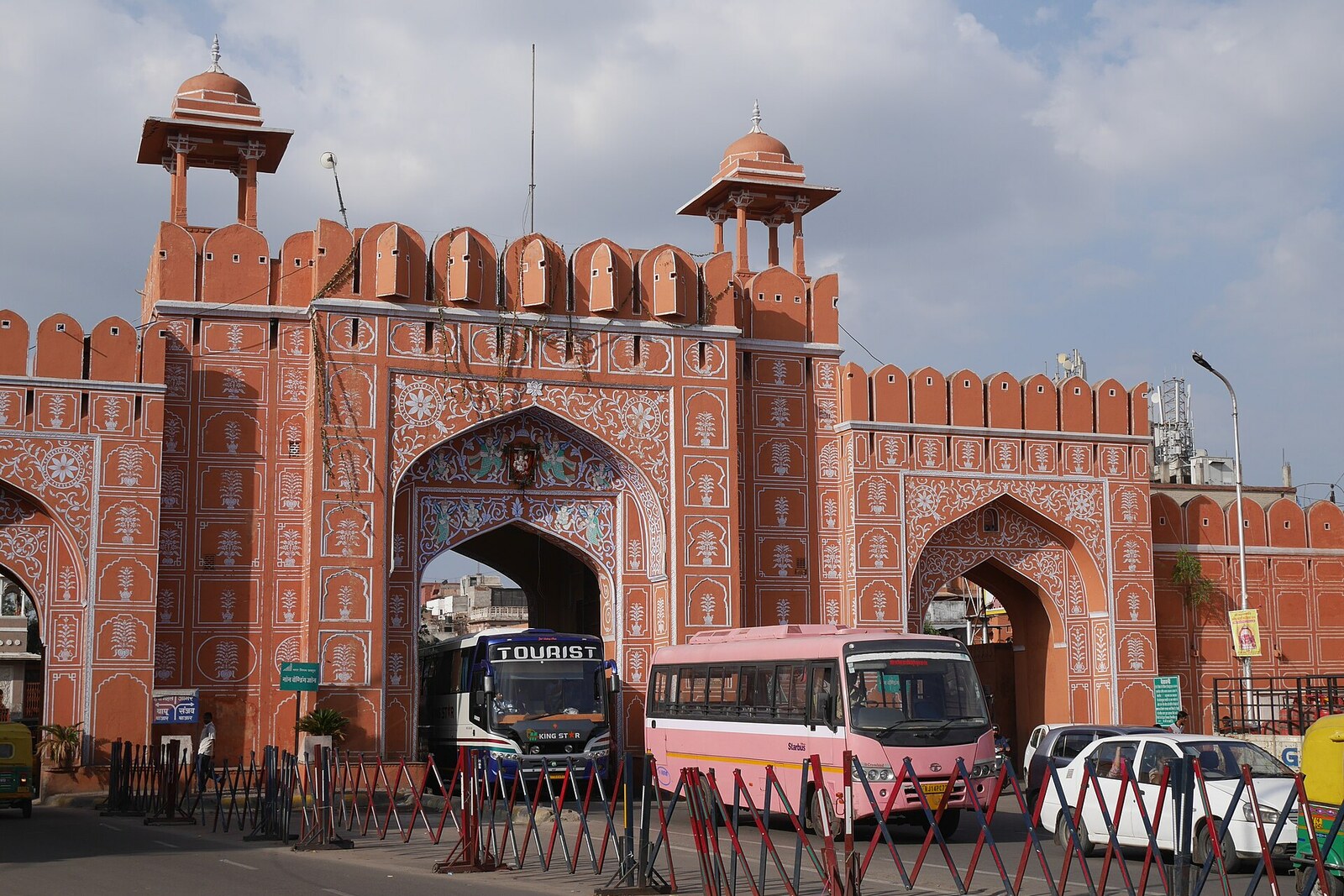 Three pink arches of Sanganeri Gate, with intricate painting and projecting battlements, against a blue sky.