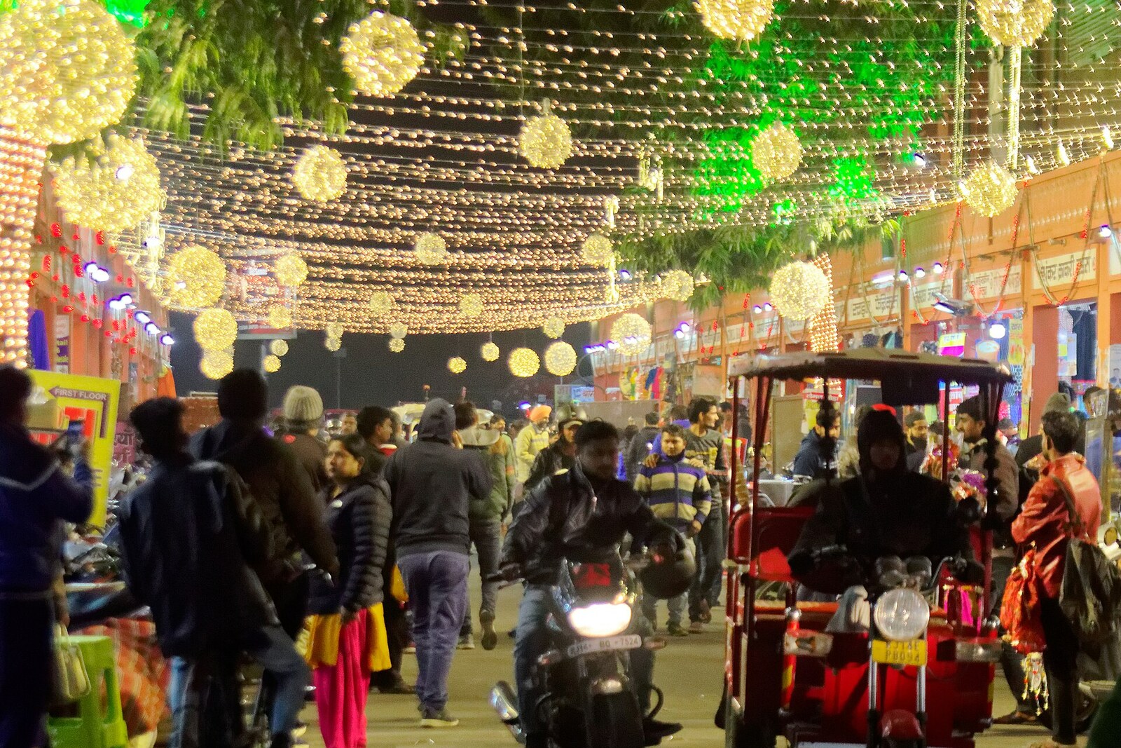Rangée rose de boutiques du Bapu Bazar à la lumière des guirlandes et des lanternes ; des ampoules sont suspendues au-dessus de la rue.