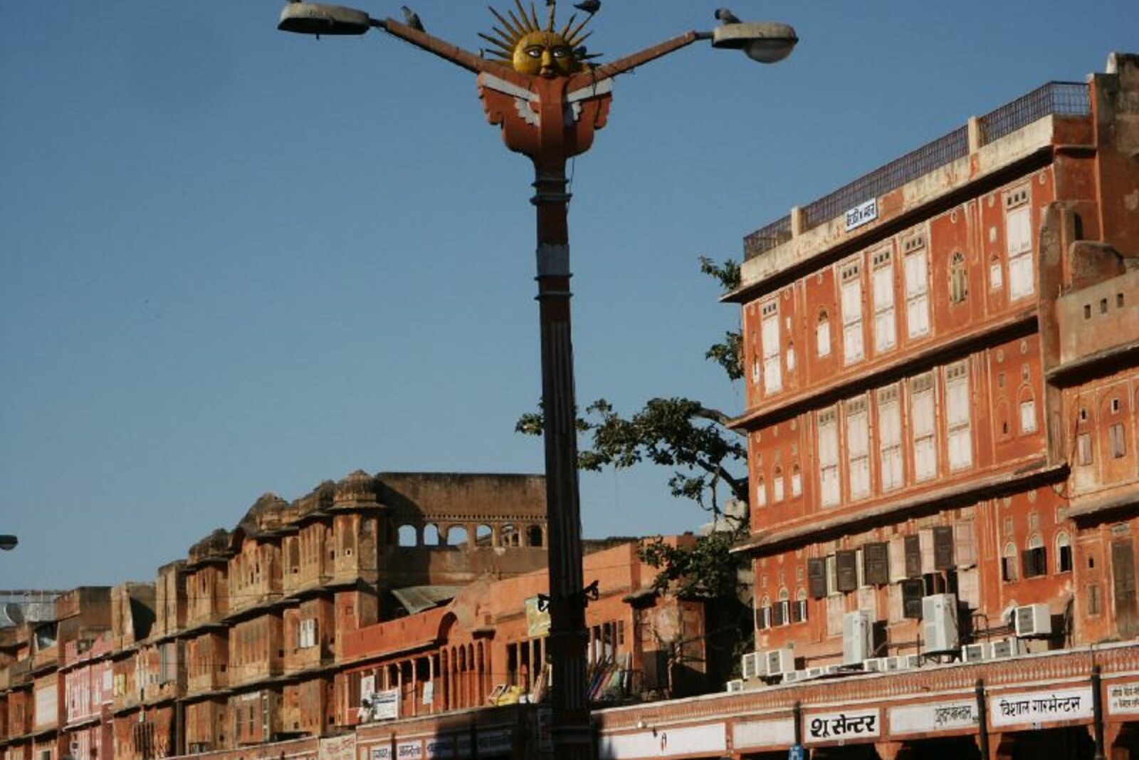Pink facades and carved balconies of Johari Bazaar, decorated with light bulbs and flags, with a streetlamp in the foreground.