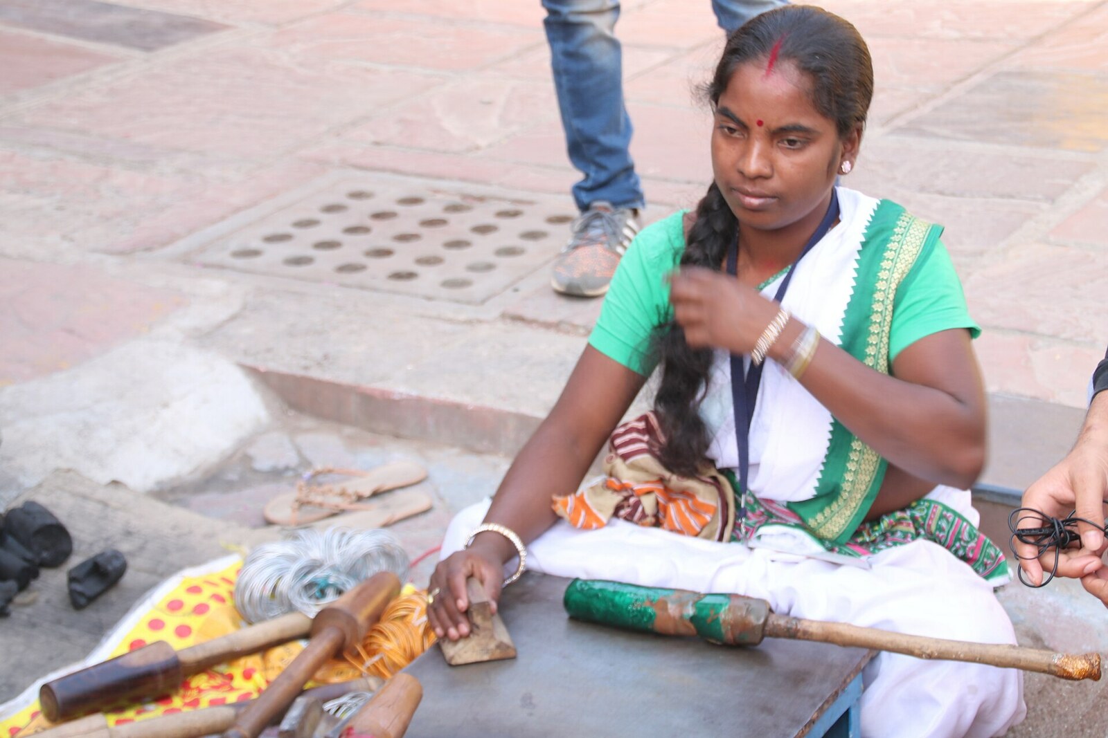 A woman in traditional clothing heats colored lacquer and rolls strips for bangles over an open brazier.