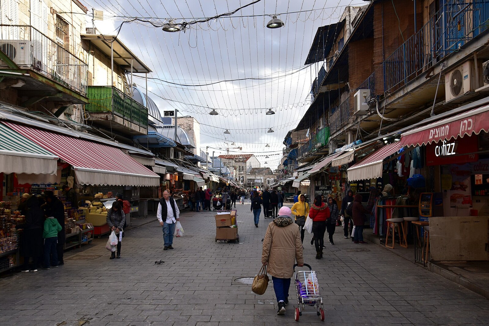 A covered street in Mahane Yehuda Market with rows of stalls, lit by hanging lamps