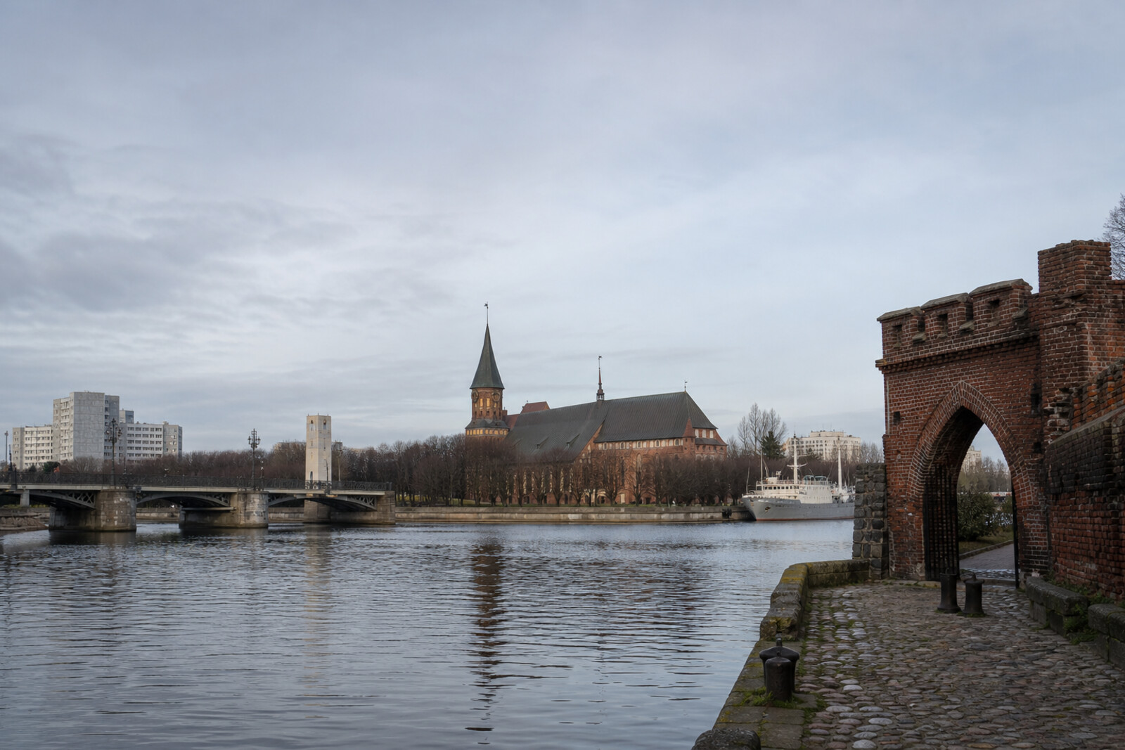 An illustrative composition of Königsberg Cathedral, a bridge, brick gates, an estacade, and a museum ship above the Pregolya.